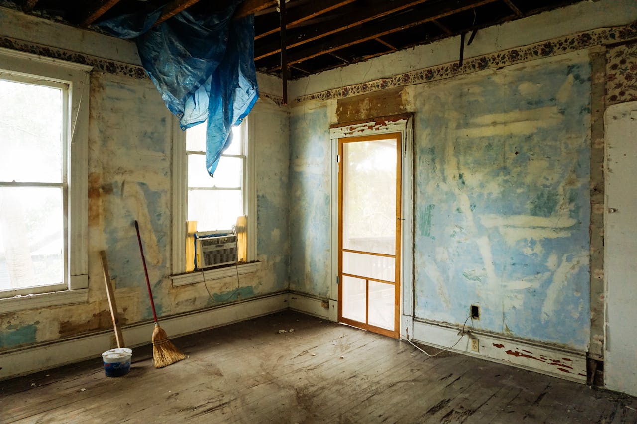 hero-img-01 An empty room in an abandoned house with peeling walls and construction tools.